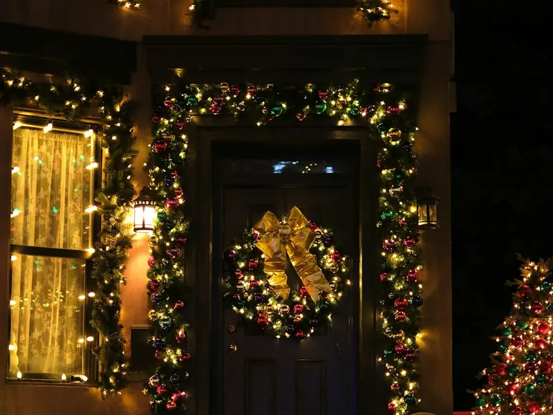Front door with a lit wreath and garland framing the entry