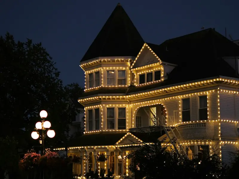 Two-story home outlined in warm white lights at dusk